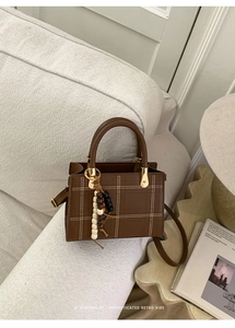 Close-up of deep brown crossbody bag with grid stitching and colorful bead charm