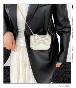 Close-up of mini white crossbody bag with leather bow and elegant pearl handle