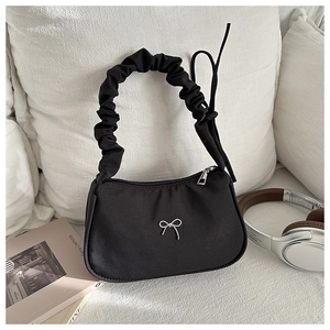 Detail of black satchel with pleated handle and silver butterfly logo on a sofa