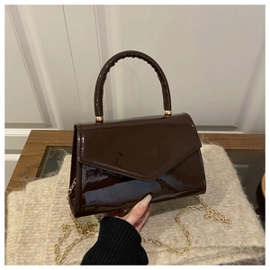 Detail of dark brown patent leather handbag with triangular flap and gold chain strap