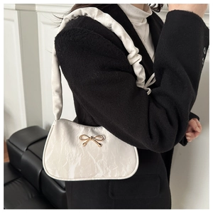 Detail of white baguette bag featuring a gold bow ornament and ruched cloud strap