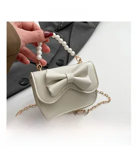 Detail of cream crossbody bag featuring a large leather bow and elegant pearl handle