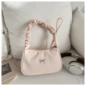 Detail of light beige hobo bag featuring pleated handle and silver metal bow ornament