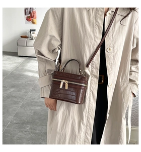 Detail of dark brown crocodile pattern box bag with golden zippers and shoulder strap