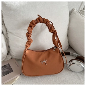 Detail of caramel brown baguette bag with silver butterfly charm on a white fabric surface