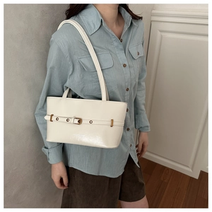 Close-up of a cream tote bag featuring stylish belt buckles and silver rivet detailing
