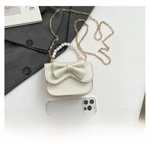 Mini pearl handle crossbody bag with bow detail and chain strap shown next to phone