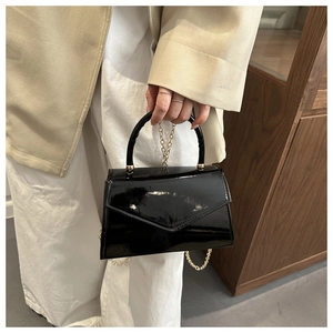 Dettaglio di borsa in vernice nera con catena dorata e design a patta stile busta