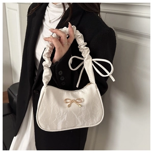 Detailed view of white pleated handbag with gold butterfly accent and side ribbon bow