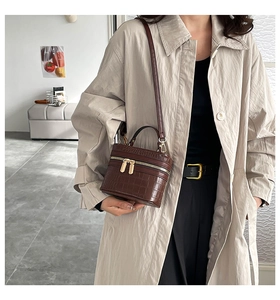 Borsa a scatola marrone coccodrillo con zip dorate indossata su un trench color kaki
