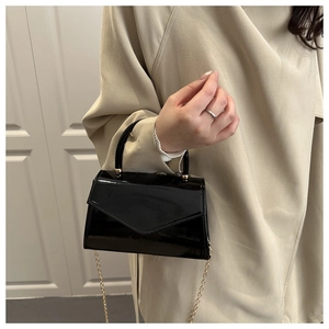 Detail of black patent leather crossbody bag with V-flap and gold chain strap on model