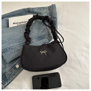 Detail of black crescent shoulder bag featuring ruched handle and silver bow accent