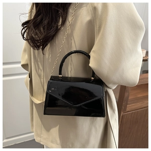 Close-up of black patent leather crossbody bag with gold hardware and chain strap details