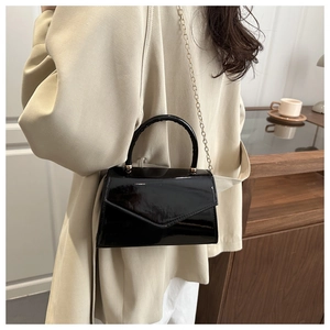 Detail of glossy black patent leather bag with gold chain strap worn with beige coat