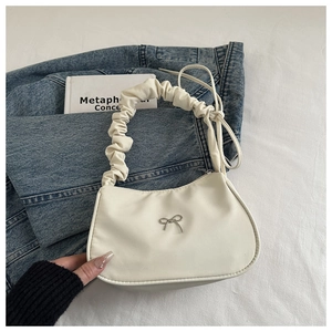Close-up of cream shoulder bag with pleated handle and silver metal bow detail