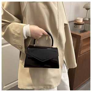 Detail of black patent leather crossbody bag with gold chain strap and round top handle