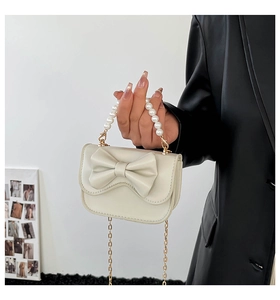 Dettaglio borsa in pelle bianco crema con fiocco grande, manico di perle e catena d'oro
