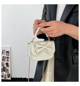 Detail of cream mini bag featuring pearl handle, bow decoration and gold chain strap