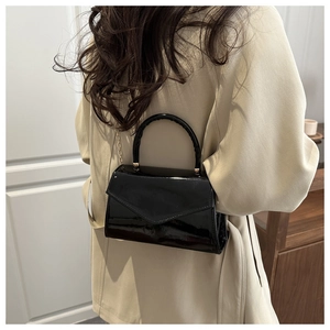 Detail of black patent leather bag with gold chain strap on cream coat