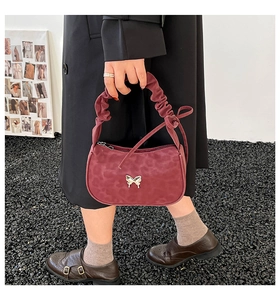 Detail of burgundy suede handbag featuring silver butterfly buckle and scrunchie handle