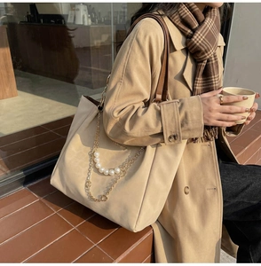 Dettaglio della borsa tote beige con catena di perle decorativa e manici in pelle marrone