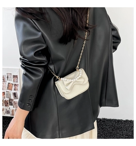 Detail of cream crossbody bag with leather bow and pearl accents on black faux leather coat