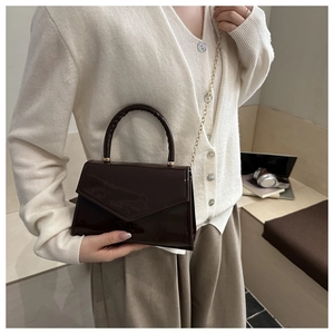 Detail of dark brown patent leather crossbody bag with chain strap for office commute