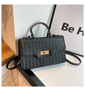 Détail d'un sac à main tissé noir avec fermoir rotatif doré et poignée supérieure robuste