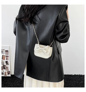 Detail of cream mini bow bag with pearl handle worn over a black leather blazer
