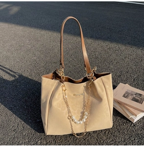 Detail shot of beige tote bag with brown straps and elegant pearl chain on asphalt surface