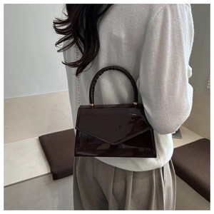 Detail of a shiny dark brown patent leather mini square bag with a metallic chain strap