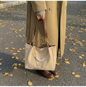 Detail of beige tote bag with pearl chain accessory and golden hardware on leather handle