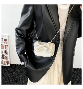 Detail view of cream white mini crossbody bag with pearl handle and bow decoration