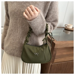 Detail of green crescent bag featuring a metallic bow and pleated handle with ribbons