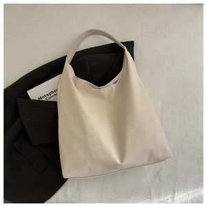 Close-up of cream leather tote bag on textured background with black blazer detail