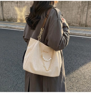 Dettaglio di borsa tote in pelle scamosciata beige con catena di perle e tracolla