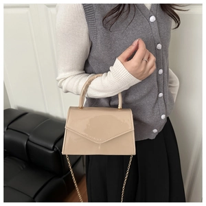 Detail of a beige glossy patent leather handbag with a sleek envelope flap and gold chain