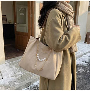 Detail of beige tote bag with gold chains, white pearls and a clover charm in snow setting