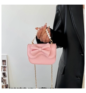 Pink mini crossbody bag featuring a large bow, pearl handle and gold chain strap