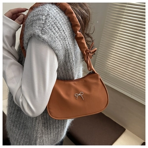 Detail of caramel shoulder bag with pleated strap and silver bow on textured fabric
