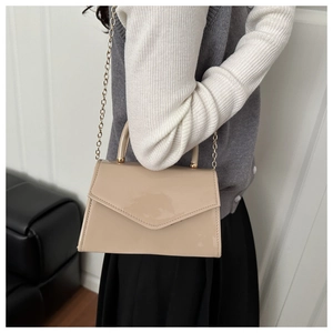 Detail of nude beige patent leather crossbody bag with gold chain and top handle