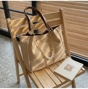 Dettaglio di una borsa tote beige con catena di perle e manici marroni in luce soffusa