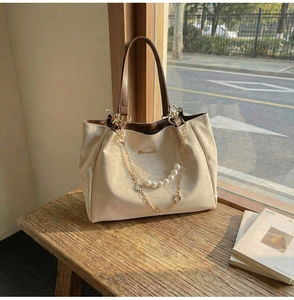 Detail of cream tote bag featuring pearl chain accents and floral gold charms on wood