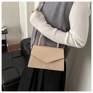 Close-up of a beige envelope shoulder bag with gold metal handle on a model