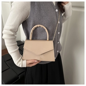 Borsa a mano beige in vernice con manico a pieghe e catena d'oro su una modella