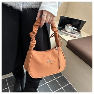 Detail of the orange crescent shoulder bag with a silver metal bow and ruched handle