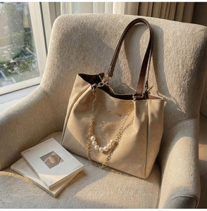 Detail of cream tote bag with large white pearl chain and brown leather strap on chair