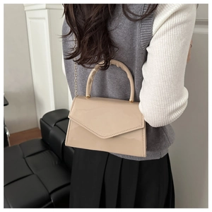 Close-up of beige patent leather bag with gold chain and pleated handle on a model