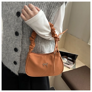 Detail of orange nylon dumpling bag with pleated handle and silver bow accent