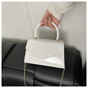 Detail of glossy white patent leather handbag with gold chain strap and curved handle